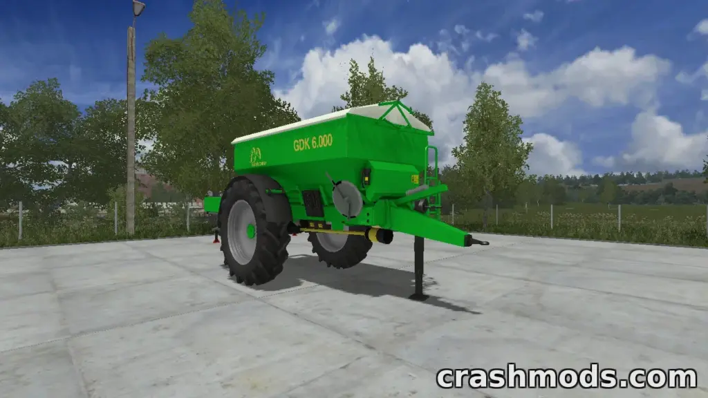 The Güstrower GDK 6000 mod features a green fertilizer spreader parked on a farmyard, surrounded by trees and a clear sky.