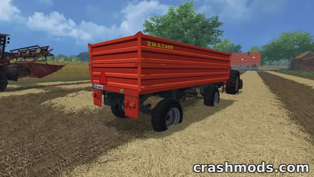 The Zmaj 489 trailer is parked on a farm road, showcasing its vibrant orange design and sturdy build.
