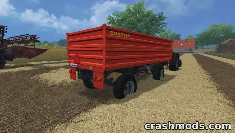 The Zmaj 489 trailer is parked on a farm road, showcasing its vibrant orange design and sturdy build.