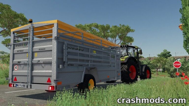 Joskin Betimax RDS 6000 livestock trailer attached to a tractor, set in a vibrant farming landscape.